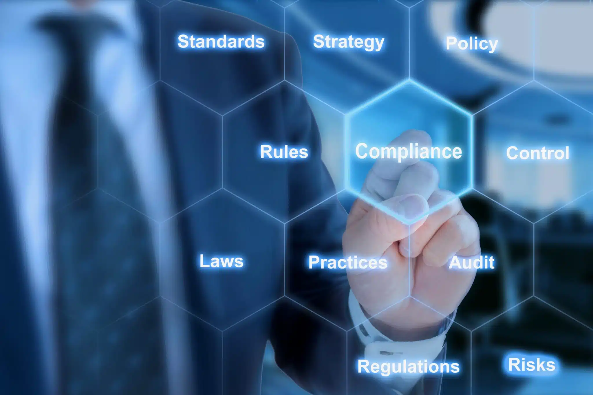 Businessman in Blue Suit in Front of Office Background Clicking Tile with the Word Compliance in Hexagon Grid - KX